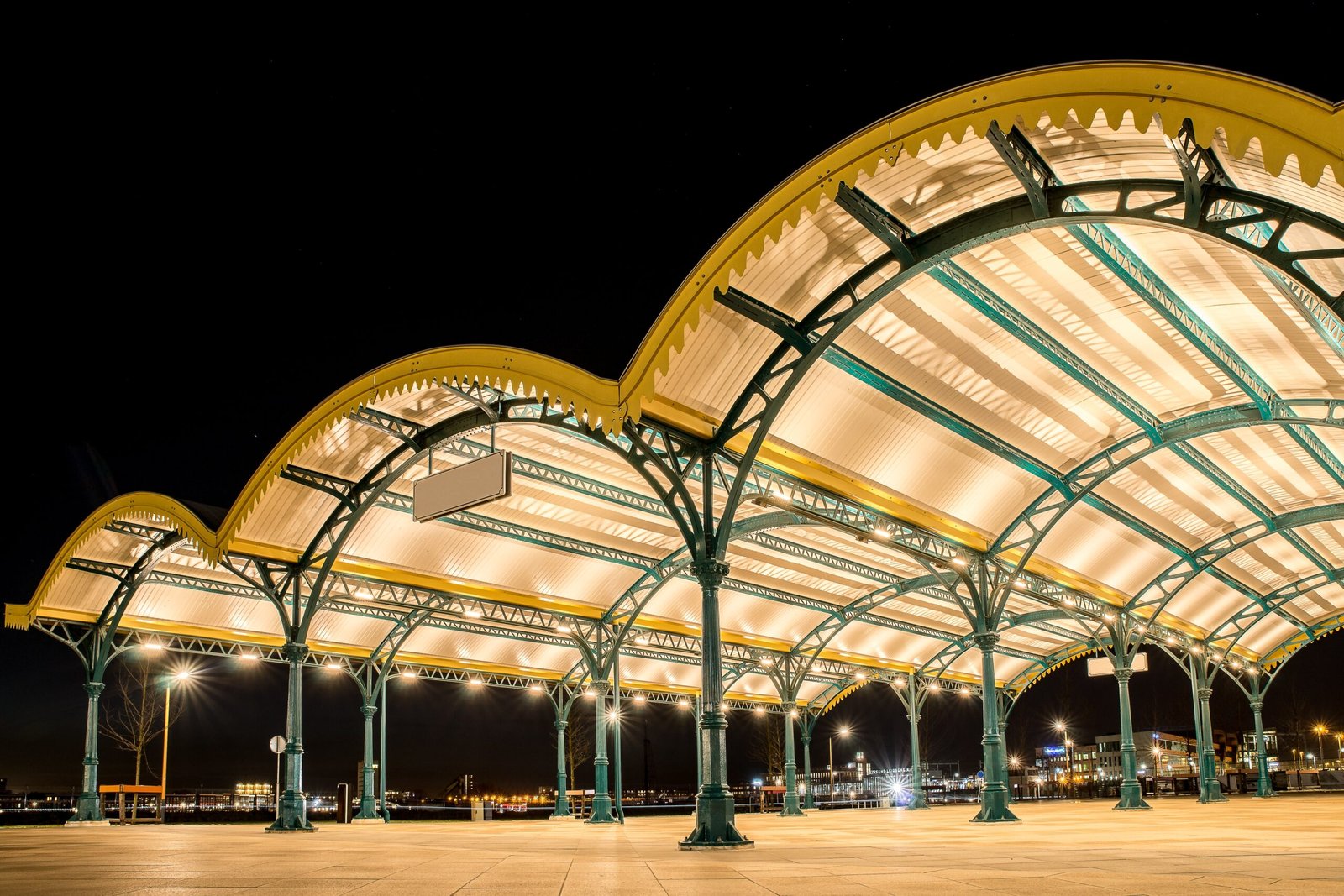 Angled shot of three yellow curved roofs in a city with lights under a dark sky